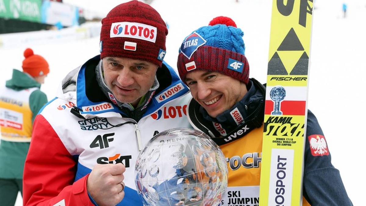 Dwóch mężczyzn w strojach narciarskich, jeden z nich trzyma szklaną kulę, obaj uśmiechnięci.