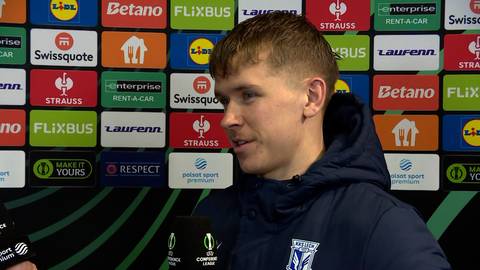 Antoni Kozubal, młody piłkarz, w wywiadzie po meczu, na tle ścianki z logotypami sponsor&oacute;w.