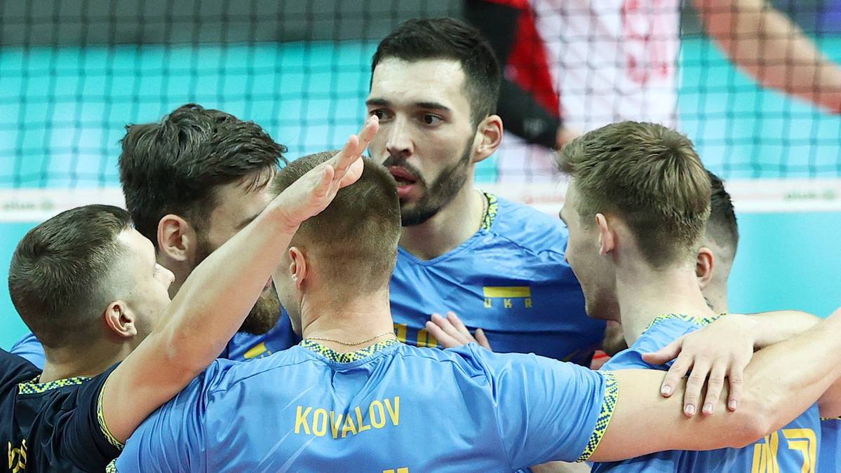 Grupa zawodników drużyny siatkarskiej w niebieskich koszulkach z żółtymi elementami, otaczająca siebie w geście mobilizacji.