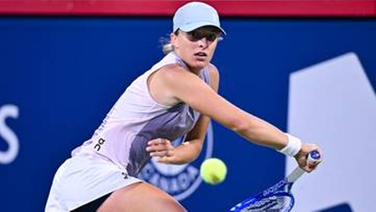 Iga Świątek podczas meczu tenisowego uderza piłkę rakietą.