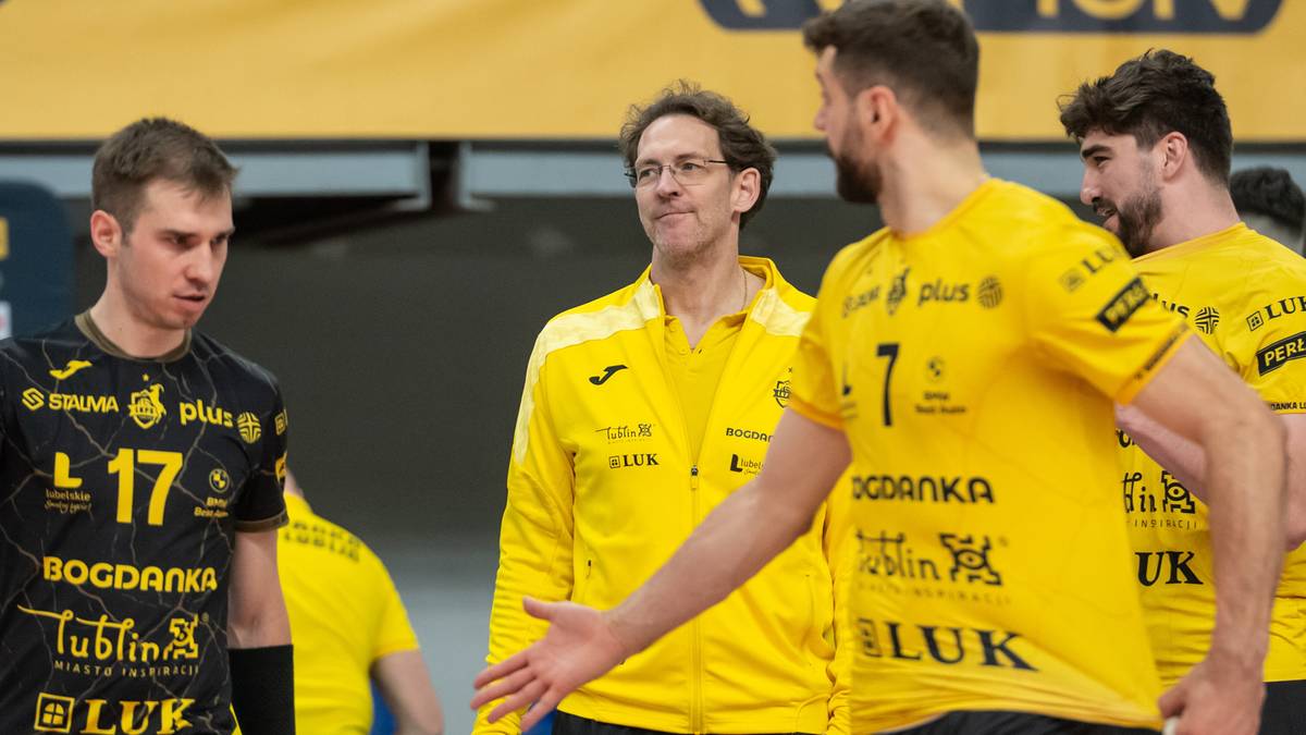 Siatkarze w ż&oacute;łtych strojach z numerami na plecach stoją na boisku, jeden z nich rozmawia z trenerem.