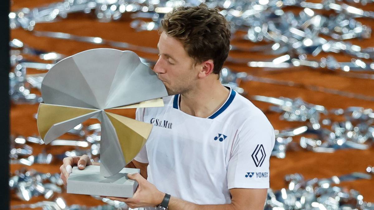 Mężczyzna w białej koszulce z logo trzyma puchar i całuje go.