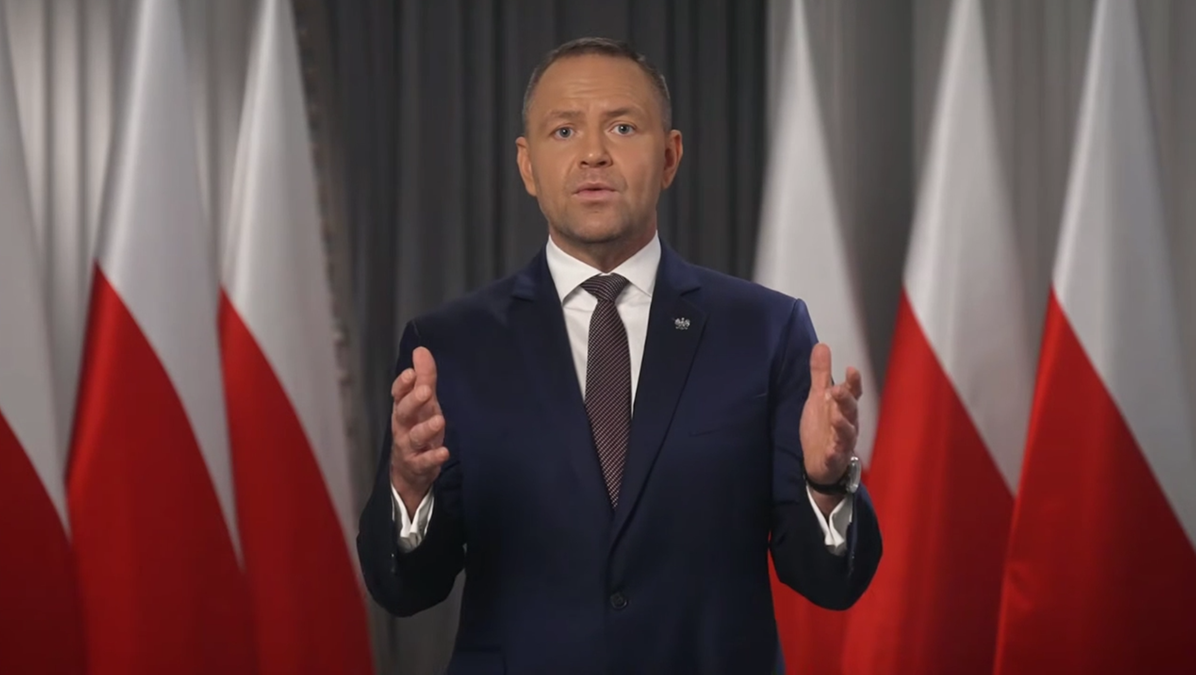 Prezydent Karol Nawrocki przemawia na tle polskich flag.