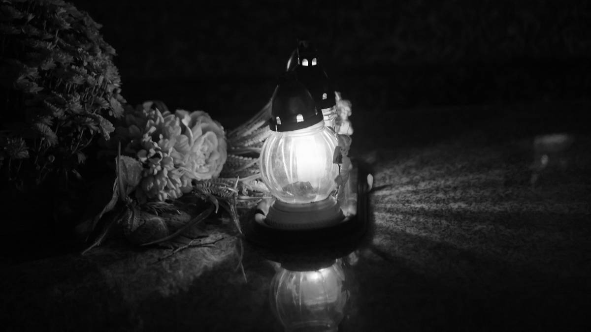 Płonący znicz z kwiatami w tle, symbol żałoby.