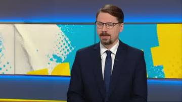 Mężczyzna w okularach, granatowym garniturze i krawacie stoi przed kolorowym tłem.