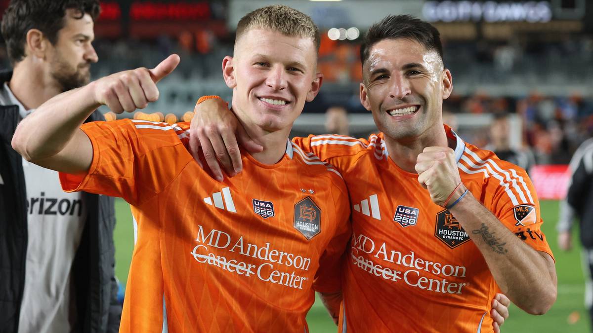 Dwóch piłkarzy w pomarańczowych koszulkach Houston Dynamo, jeden pokazuje kciuk w górę, obaj uśmiechnięci.