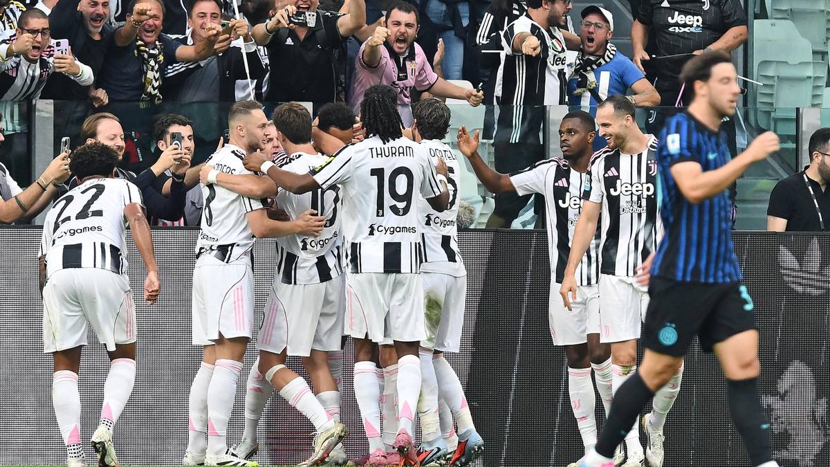 Piłkarze w białych strojach z czarnymi pasami świętują po strzelonej bramce. Widoczny numer 22 na plecach jednego z graczy, tłum kibiców w tle.