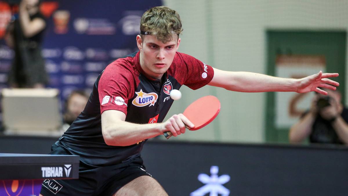 Młody zawodnik tenisa stołowego w akcji podczas meczu, uderzający piłeczkę rakietką.