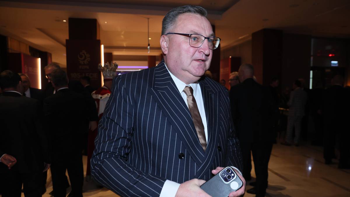 Mężczyzna w garniturze w paski i okularach, trzymający smartfon.