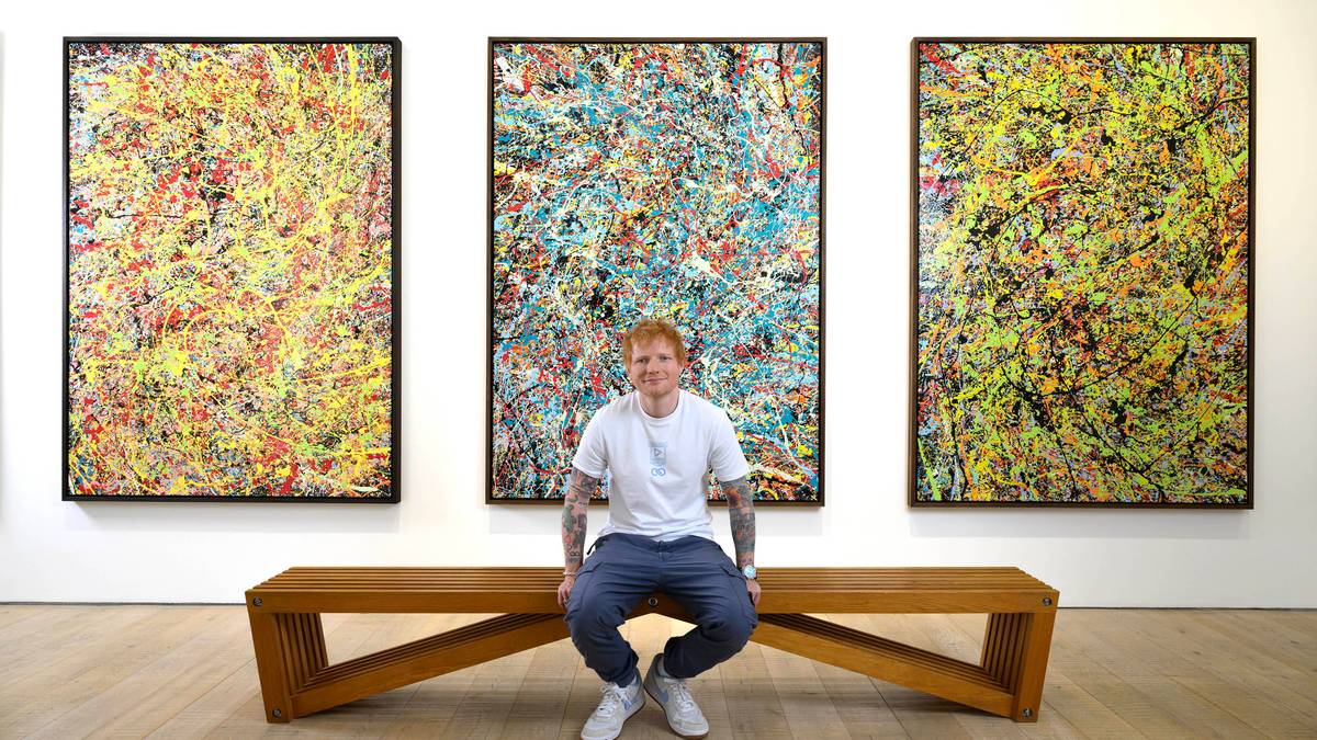 Ed Sheeran siedzi na ławce w galerii sztuki, przed trzema abstrakcyjnymi obrazami.
