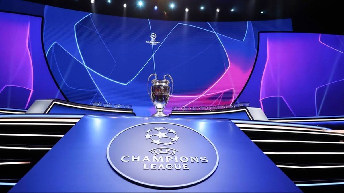 Puchar Ligi Mistrzów UEFA stoi na podeście. W tle widoczny jest duży ekran z logotypem Champions League i niebiesko-fioletowym oświetleniem.