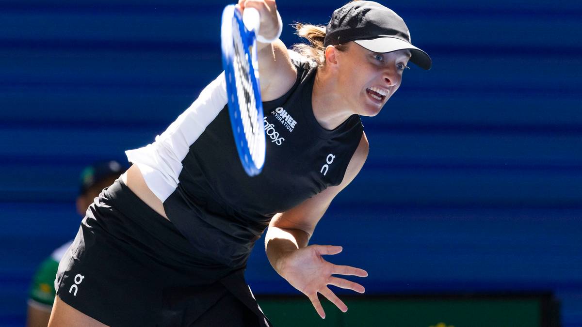 Graczka Iga Świątek podczas meczu tenisowego, uderza piłkę rakietą. Ma na sobie czarny top i spódnicę, a na głowie czapkę.