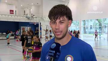 Jakub Czarnecki udziela wywiadu na tle hali sportowej, w kt&oacute;rej trenują młodzi siatkarze.