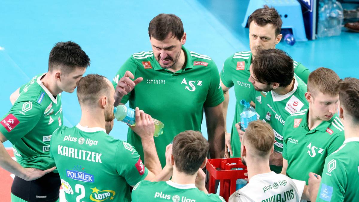 Grupa siatkarzy w zielonych strojach zebrana w k&oacute;łku, jeden z nich podaje butelkę z wodą.