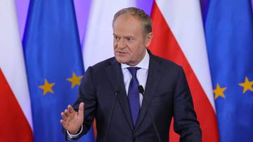 Donald Tusk przemawia na tle flag Polski i Unii Europejskiej.