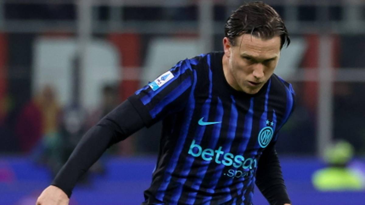 Piłkarz Piotr Zieliński w niebiesko-czarnej koszulce kopie piłkę na boisku.