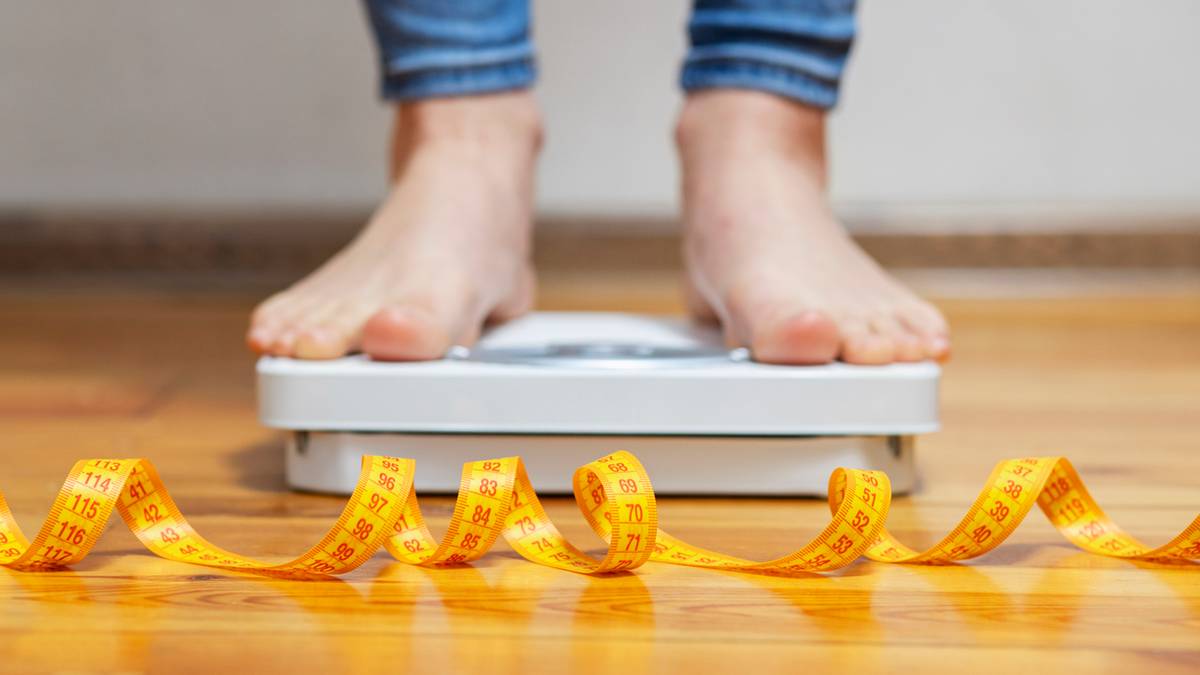 Osoba stoi na wadze łazienkowej z centymetrem krawieckim przed nią.