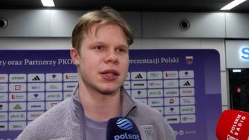 Michał Niewiński udziela wywiadu przed tablicą z logotypami sponsorów i flagą Polski.