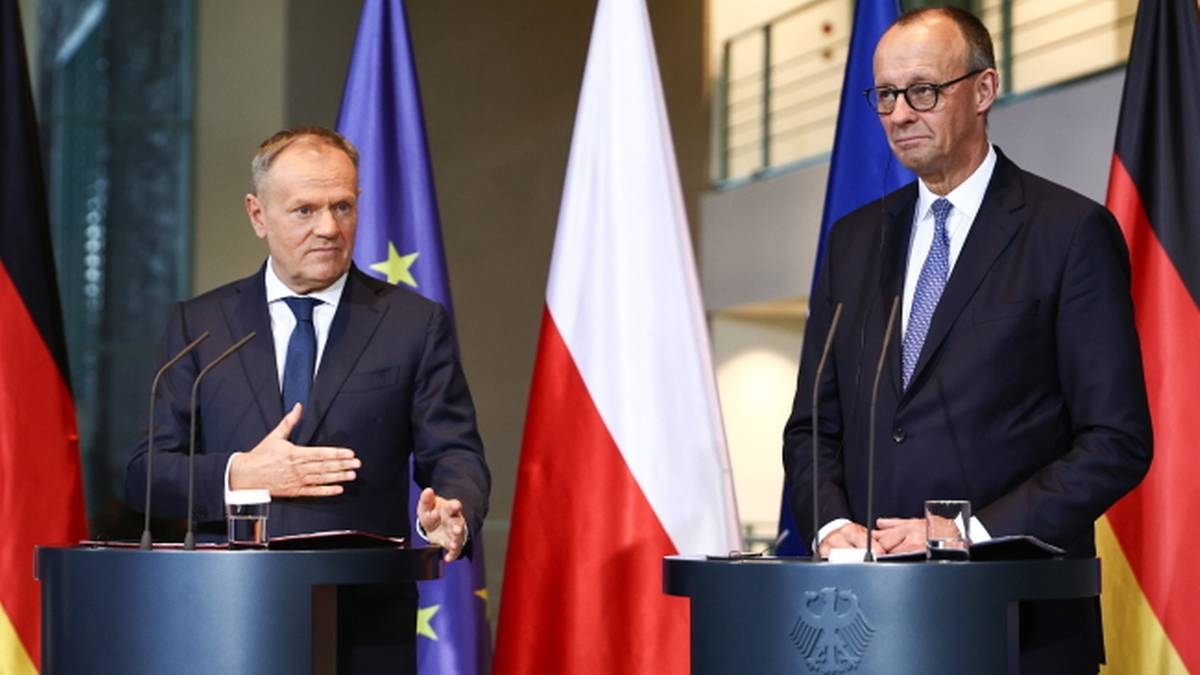 Dwóch mężczyzn w garniturach stoi za mównicami, z flagami Polski i Niemiec w tle.