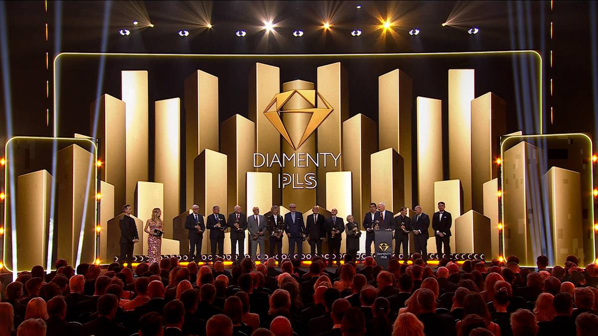 Grupa os&oacute;b na scenie podczas ceremonii wręczenia nagr&oacute;d, na tle złotej scenografii z logo "DIAMENTY PLUS".