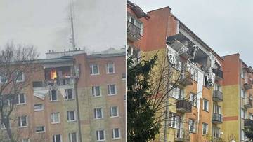 Uszkodzony blok mieszkalny po eksplozji, widoczne wyrwane ściany i balkony, dym unoszący się z jednego z mieszkań.