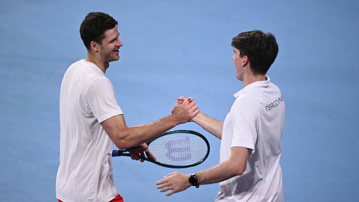 Dwóch tenisistów ściska sobie dłonie na korcie, jeden z nich trzyma rakietę.