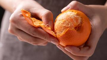 Dłonie obierające pomarańczę, odsłaniające jej miąższ.