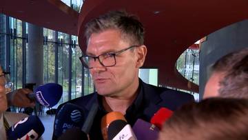 Adam Korol w okularach udzielający wywiadu w otoczeniu mikrofon&oacute;w dziennikarskich