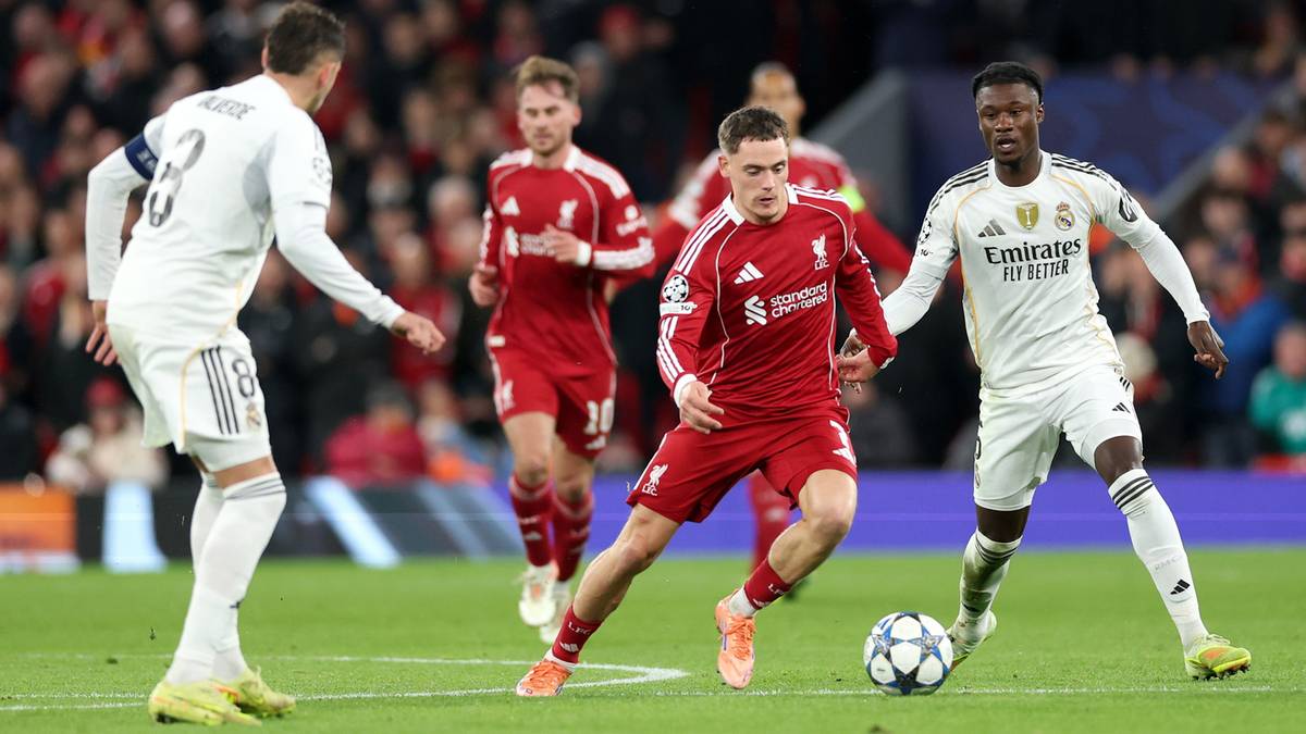 Piłkarze w czerwonych i białych strojach walczą o piłkę na boisku piłkarskim.