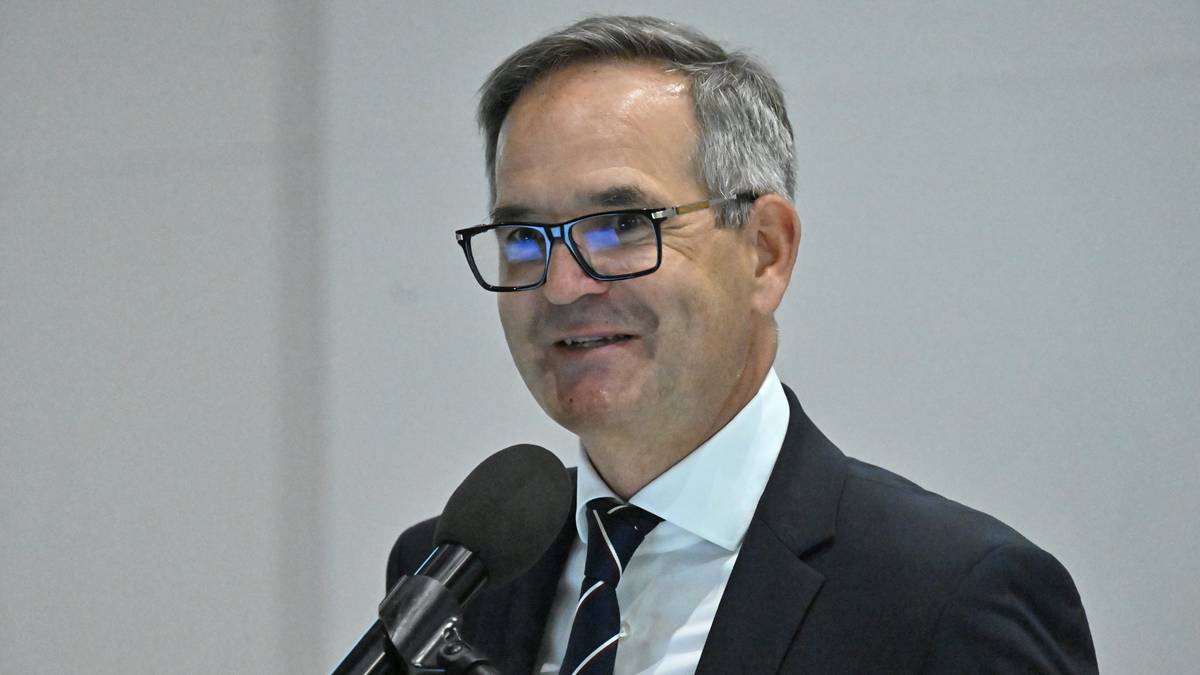 Mężczyzna w okularach i garniturze przemawia przy mikrofonie.