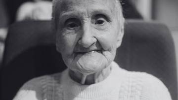 Portret Anny Kurek, uczestniczki Powstania Warszawskiego, kobiety w podeszłym wieku, ubranej w jasny sweter, z przypiętym do piersi medalem.