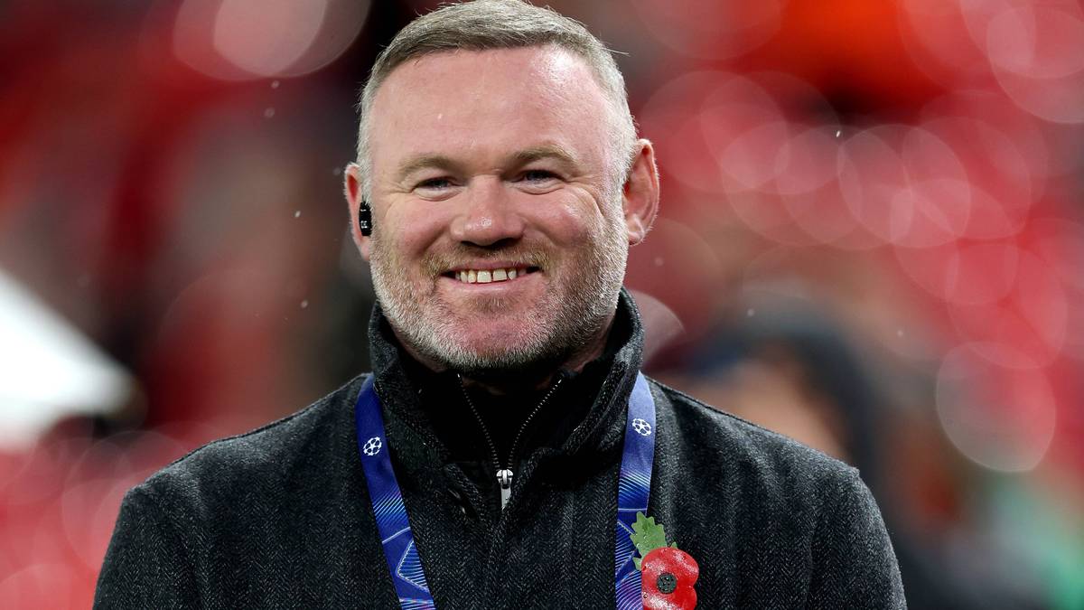 Wayne Rooney uśmiecha się, nosząc przypinkę z makiem na klapie marynarki.