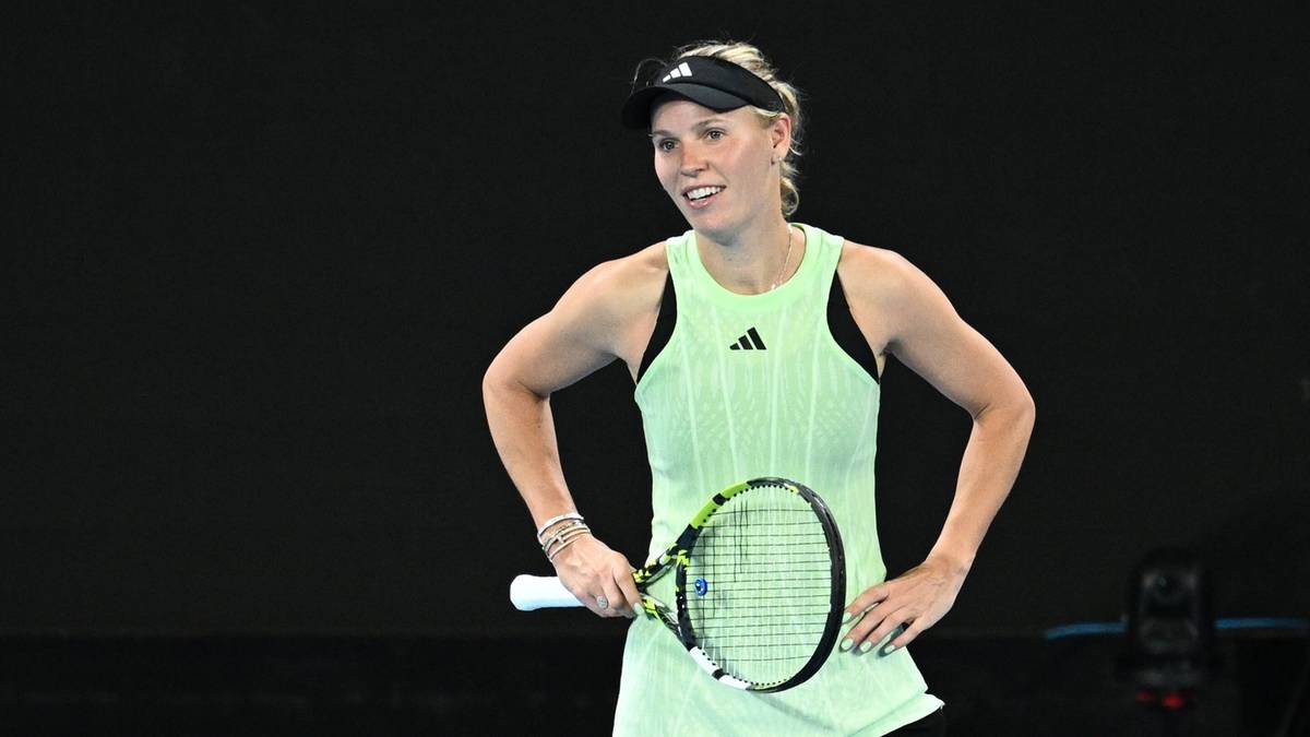 Caroline Wozniacki, duńska tenisistka polskiego pochodzenia, stoi na korcie z rakietą tenisową, ubrana w jasnozielony strój sportowy.