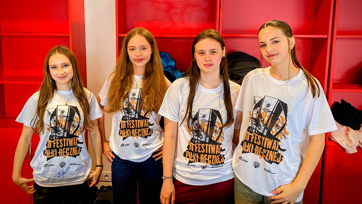 Cztery młode dziewczyny w białych koszulkach z nadrukiem festiwalu stoją obok siebie, uśmiechając się do aparatu.