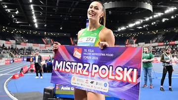 Uśmiechnięta zawodniczka lekkoatletyczna trzyma transparent z napisem "MISTRZ POLSKI" na stadionie.