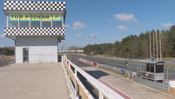 Wieża kontrolna na torze wyścigowym z napisem "TOR POZNAŃ", obok toru wyścigowego z bandami i drzewami w tle.