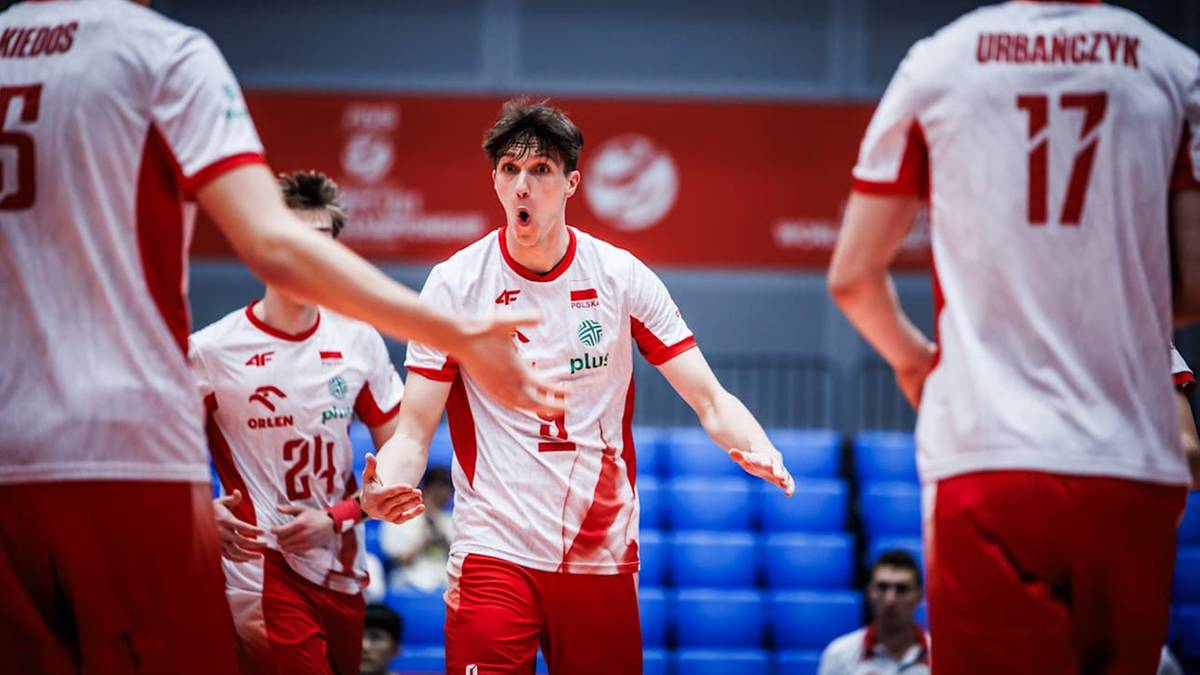 Siatkarz w białej koszulce z czerwonymi detalami, z numerem 11, na tle innych zawodników i niebieskich band.