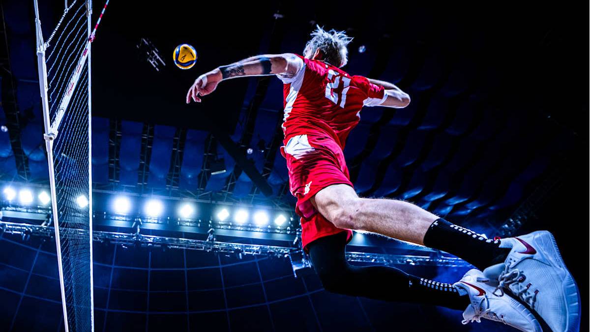 Siatkarz w czerwonej koszulce wykonuje atak nad siatką, prezentując dynamiczny ruch w powietrzu.