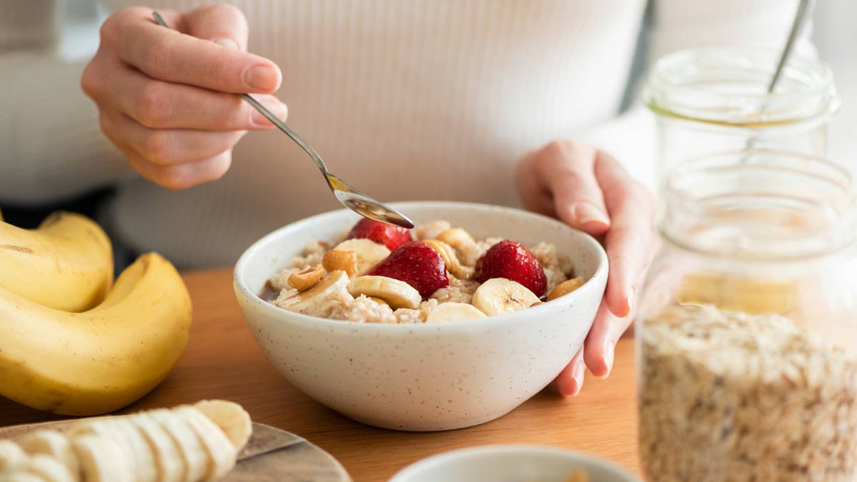 Osoba jedząca owsiankę z owocami i orzechami.