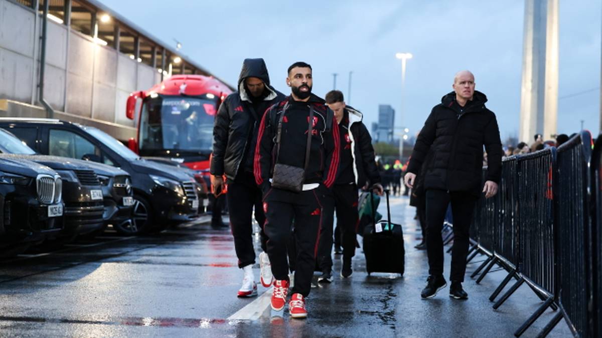 Piłkarze Liverpoolu idący w kierunku stadionu, jeden z nich niesie torbę sportową.