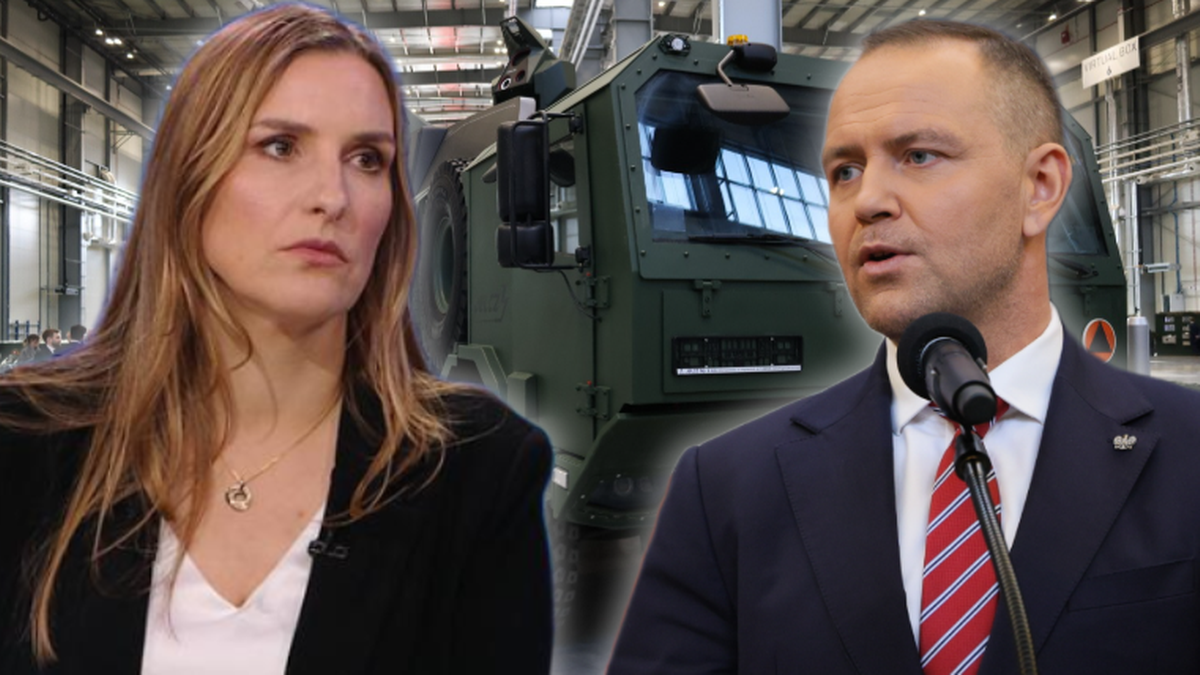 Zdjęcie przedstawia dwie osoby: po lewej stronie kobieta w czarnej marynarce, po prawej mężczyzna w garniturze z krawatem. W tle widoczny jest fragment pojazdu wojskowego.