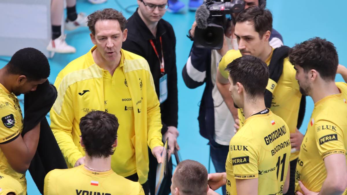Grupa siatkarzy w żółtych koszulkach otacza trenera, dyskutując.
