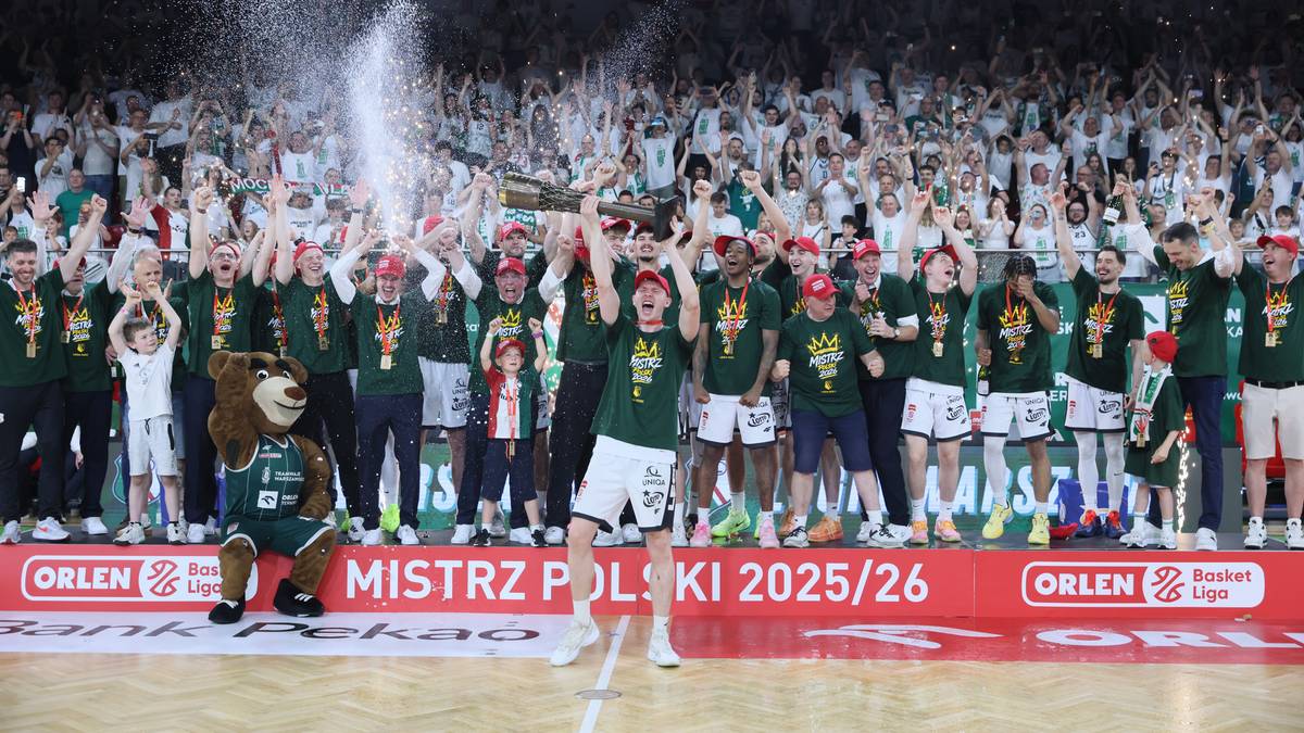 Drużyna koszykarzy w zielonych strojach świętuje zwycięstwo na podium, podnosząc puchar. Na trybunach widać licznych kibic&oacute;w, a na froncie podium znajduje się baner z napisem "MISTRZ POLSKI 2025/26".