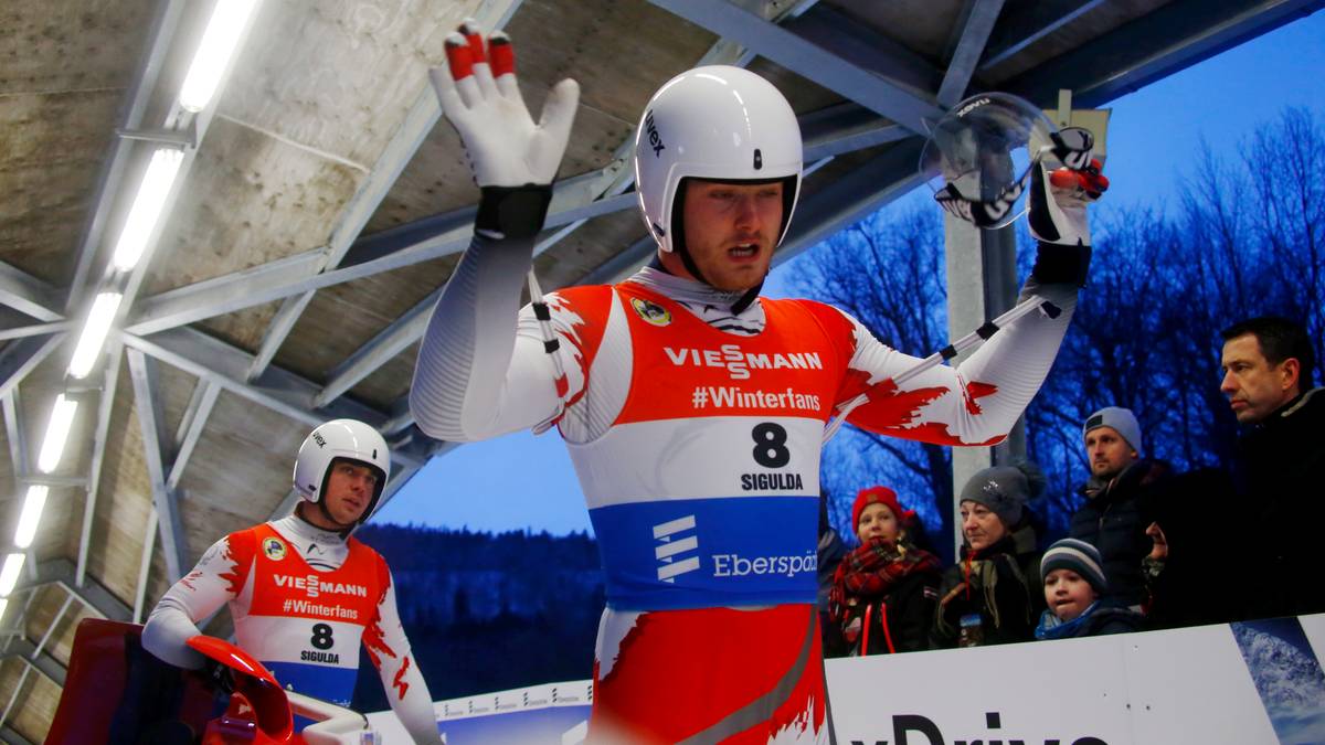 Dwóch saneczkarzy w biało-czerwonych strojach z numerami startowymi na torze.