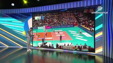 Mężczyzna w garniturze stoi przed dużym ekranem wyświetlającym mecz siatk&oacute;wki.