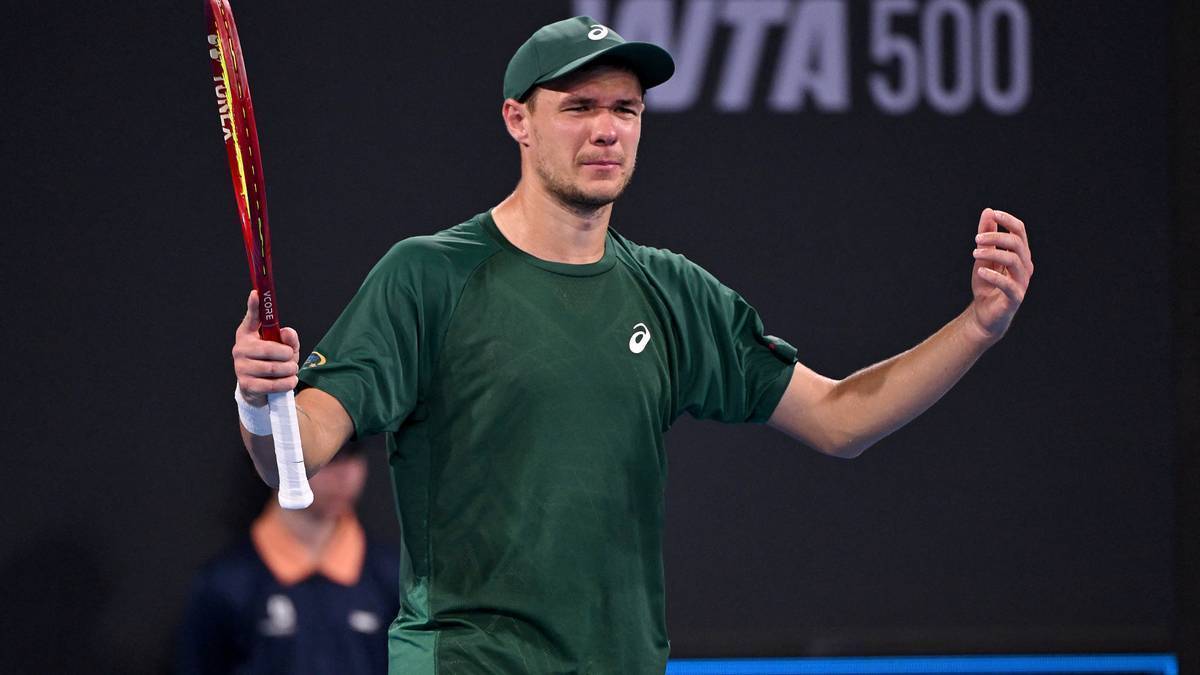 Polski tenisista Kamil Majchrzak w zielonej koszulce i czapce, trzymający rakietę, świętuje zwycięstwo na korcie tenisowym.