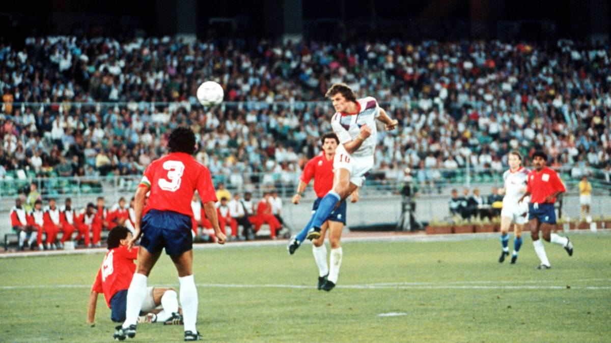Piłkarz wyskakuje do strzału głową na tle stadionu pełnego widz&oacute;w.