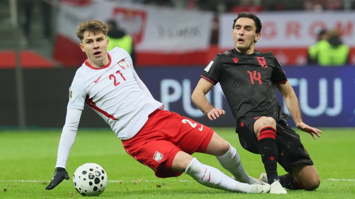 Piłkarz w białej koszulce z numerem 21 walczy o piłkę z zawodnikiem w czarnej koszulce z numerem 14.