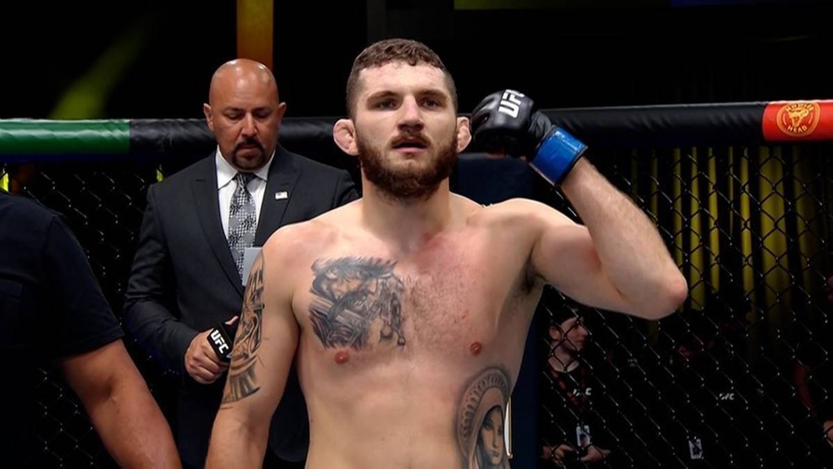 Zawodnik MMA w rękawicach bokserskich i z tatuażami na klatce piersiowej stoi w ringu.