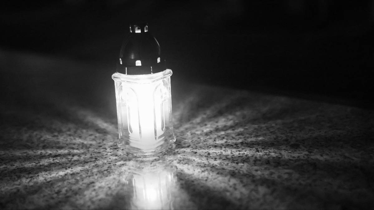 Znicz z płomieniem, rzucający cień na kamienną powierzchnię.